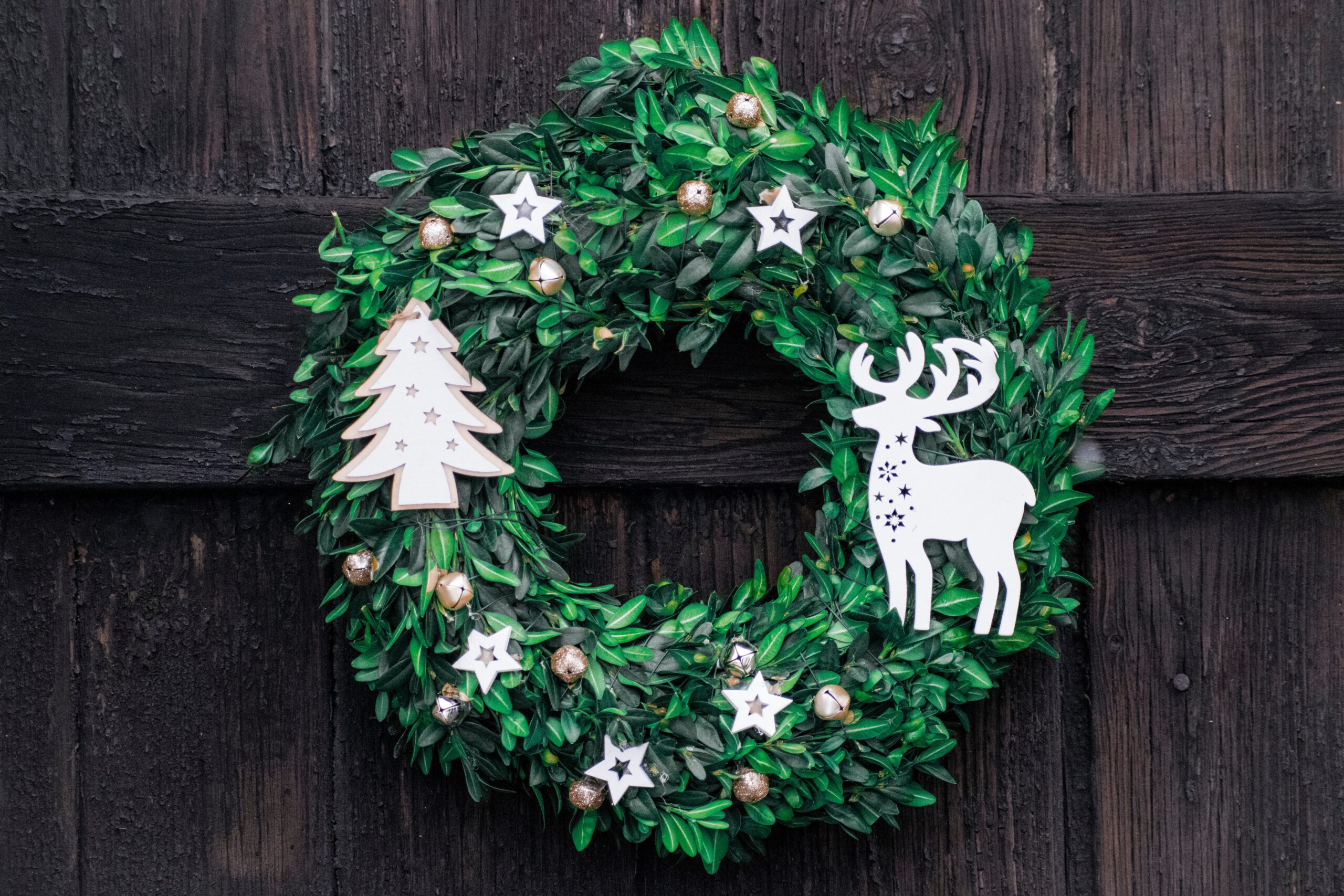 Zielony wieniec świąteczny z bukszpanu z przypiętymi dekoracjami wiszący na drzwiach
